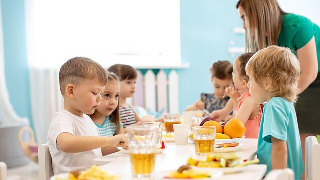 Eine Gruppe von Kindergartenkindern sitzt an einem Tisch und isst. 