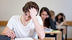 Ein Schüler sitzt an einem Tisch und fasst sich anscheinend verzweifelt in die Haare.