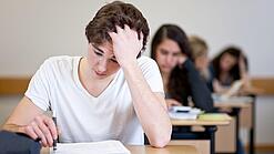 Ein Schüler sitzt an einem Tisch und fasst sich anscheinend verzweifelt in die Haare.