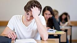 Ein Schüler sitzt an einem Tisch und fasst sich anscheinend verzweifelt in die Haare.