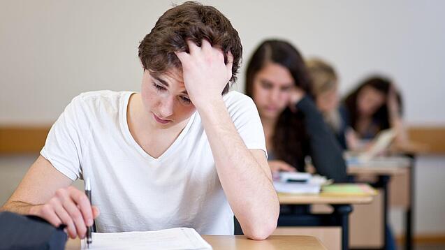 Ein Schüler sitzt an einem Tisch und fasst sich anscheinend verzweifelt in die Haare.