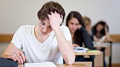 Ein Schüler sitzt an einem Tisch und fasst sich anscheinend verzweifelt in die Haare.