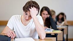 Ein Schüler sitzt an einem Tisch und fasst sich anscheinend verzweifelt in die Haare.