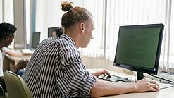 Ein junger Mann sitzt an einem Schreibtisch in einem Klassenzimmer und arbeitet an einem Computer.