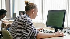 Ein junger Mann sitzt an einem Schreibtisch in einem Klassenzimmer und arbeitet an einem Computer.