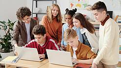 Mehrere Kinder sitzen und stehen hinter einem Tisch mit zwei Laptops.