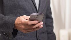 Ein Mann im Anzug hält ein Smartphone in der Hand.