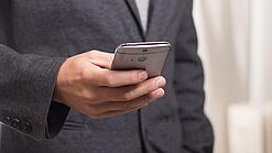 Ein Mann im Anzug hält ein Smartphone in der Hand.