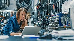 Eine junge Frau arbeitet auf einem Tisch abgestüzt an einem Laptop.
