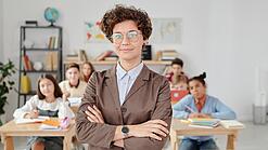 Eine Lehrerin mit Brille steht mit verschränkten Armen vor einer Schulklasse