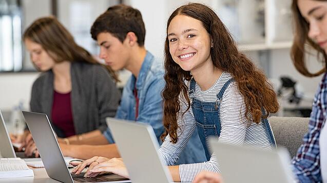 Mehrere Kinder arbeiten an aufgeklappten Laptops.