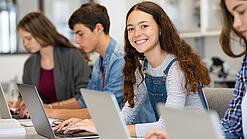 Mehrere Kinder arbeiten an aufgeklappten Laptops.