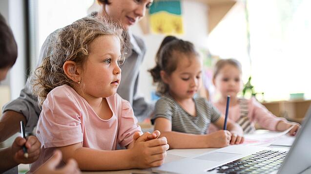 Kleinkinder und eine Frau vor einem Laptop.