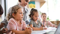 Kleinkinder und eine Frau vor einem Laptop.