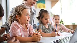 Kleinkinder und eine Frau vor einem Laptop.