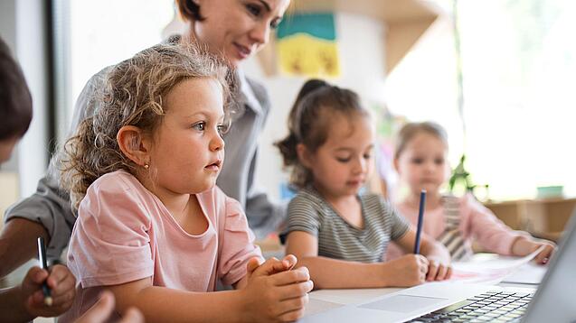 Kleinkinder und eine Frau vor einem Laptop.