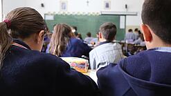 Schüler:innen sitzen in einem Klassenraum und schauen auf eine Tafel.