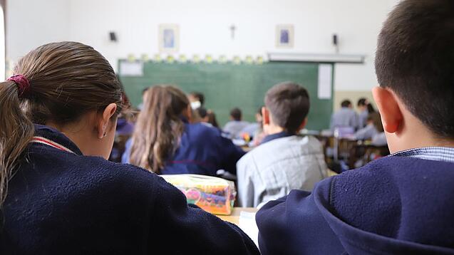 Schüler:innen sitzen in einem Klassenraum und schauen auf eine Tafel.