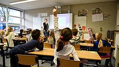 Ein Kind meldet sich im Unterricht in einem vollen Klassenzimmer.