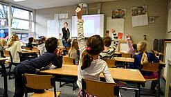 Ein Kind meldet sich im Unterricht in einem vollen Klassenzimmer.