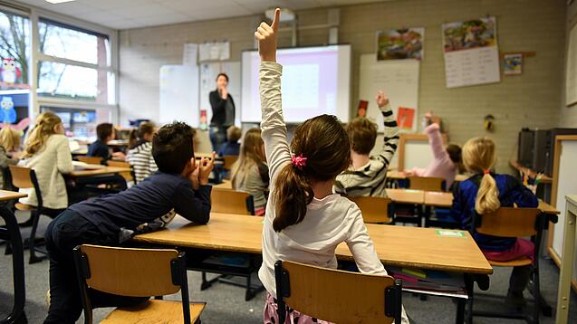 Ein Kind meldet sich im Unterricht in einem vollen Klassenzimmer.