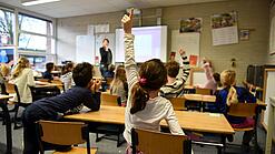 Ein Kind meldet sich im Unterricht in einem vollen Klassenzimmer.