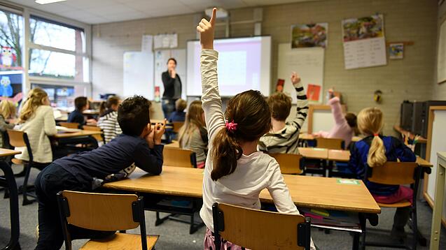 Ein Kind meldet sich im Unterricht in einem vollen Klassenzimmer.