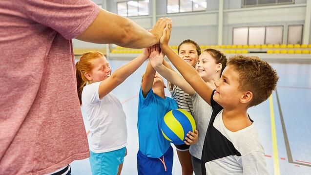 Ein Lehrer und mehrere Kinder stehen im Kreis und schlagen ein.