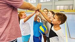 Ein Lehrer und mehrere Kinder stehen im Kreis und schlagen ein.