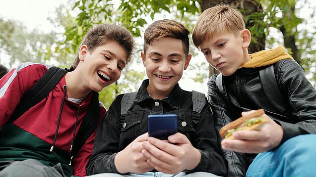 Drei Jungs sitzen um ein Smartphone und schauen darauf.