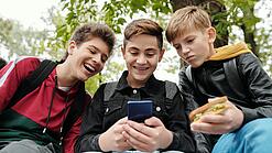 Drei Jungs sitzen um ein Smartphone und schauen darauf.
