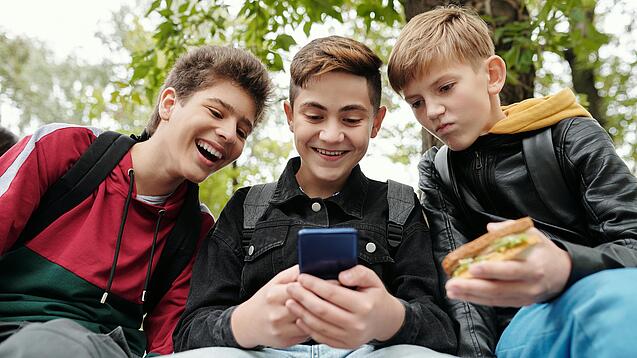 Drei Jungs sitzen um ein Smartphone und schauen darauf.