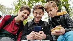 Drei Jungs sitzen um ein Smartphone und schauen darauf.