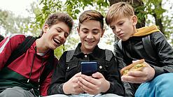 Drei Jungs sitzen um ein Smartphone und schauen darauf.