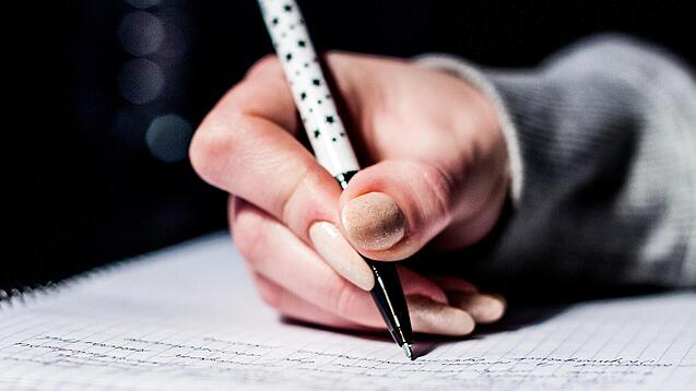 Die Hand einer Schülerin mit Stift und Block.