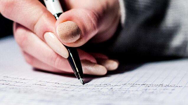 Die Hand einer Schülerin mit Stift und Block.