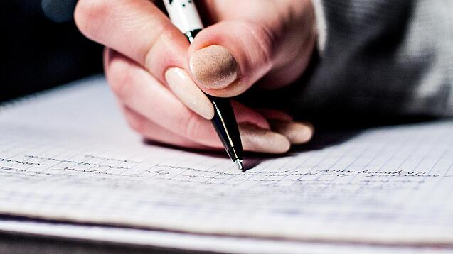 Die Hand einer Schülerin mit Stift und Block.
