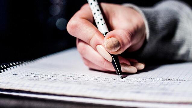Die Hand einer Schülerin mit Stift und Block.