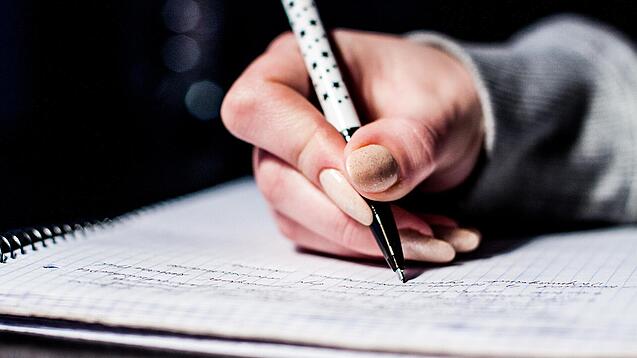 Die Hand einer Schülerin mit Stift und Block.