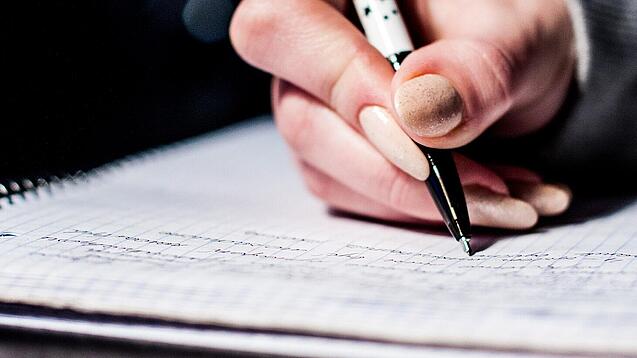 Die Hand einer Schülerin mit Stift und Block.