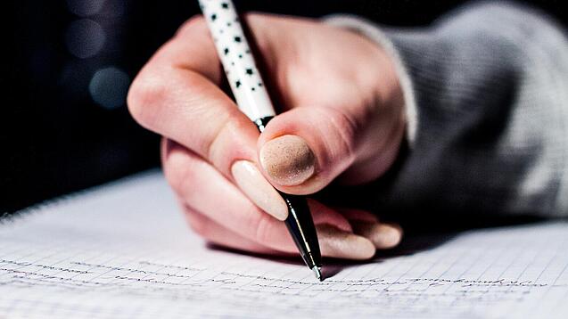 Die Hand einer Schülerin mit Stift und Block.