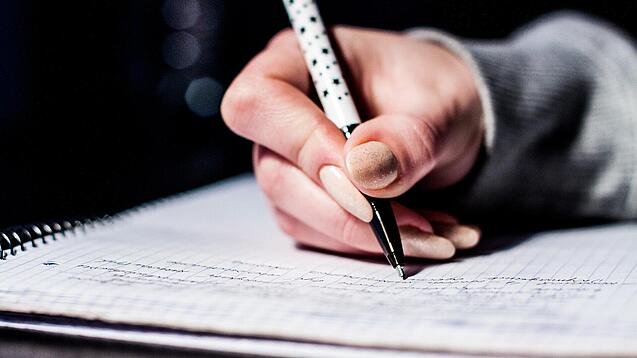 Die Hand einer Schülerin mit Stift und Block.