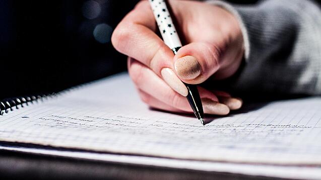 Die Hand einer Schülerin mit Stift und Block.