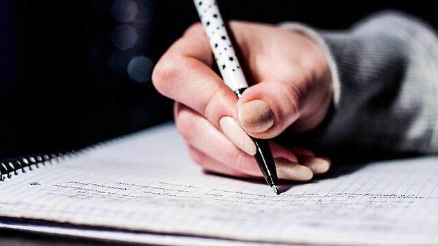 Die Hand einer Schülerin mit Stift und Block.