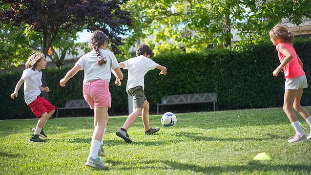 Grundschulkinder spielen Fußball auf einer Wiese.