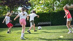 Grundschulkinder spielen Fußball auf einer Wiese.