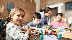 Ein Kind lächelt, während es mit anderen Kindern an einem Tisch sitzt und malt.