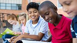 Mehrere Kinder schauen sitzend und lächelnd in Schulbücher und -hefte.