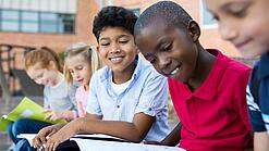 Mehrere Kinder schauen sitzend und lächelnd in Schulbücher und -hefte.