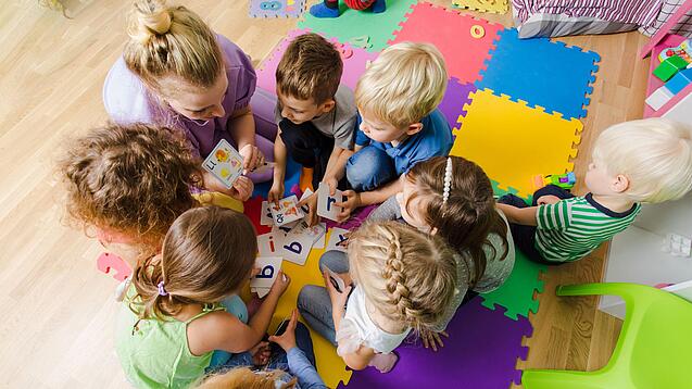 Kindergartenkinder sitzen in einem Kreis und lernen Buchstaben mit einer Erzieherin.